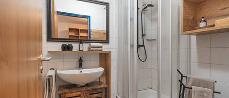 Un baño moderno con ducha envuelta en vidrio, tocador de madera con lavamanos y un espejo arriba.