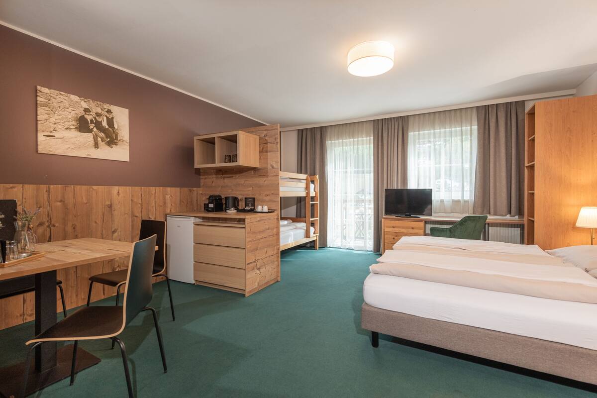 A hotel room with a wooden desk, a bed, a TV, and a window with curtains.