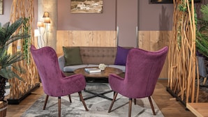 A modern lounge area with a wooden sofa, two purple armchairs, a coffee table, and a large plant. - AlpenParks Hotel Montana Matrei (Matrei in Osttirol)