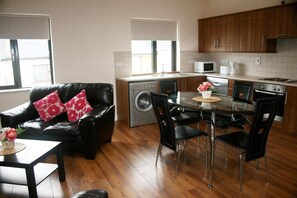 A compact living space with a dining area, a sofa with floral cushions, a washing machine, and a kitchenette.
