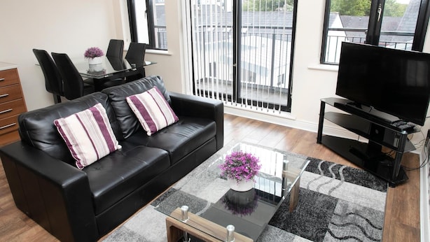 A modern living room with a black leather sofa, a glass coffee table, and a flat-screen TV. - Arch House Apartments (Athlone)