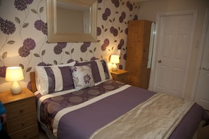 A bedroom with a bed, nightstands, a mirror, a wardrobe, and a door.