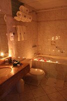 Un baño con lavamanos, inodoro y bañera de mármol. Hay toallas colgadas en la pared, un secador de pelo y un jabonera.