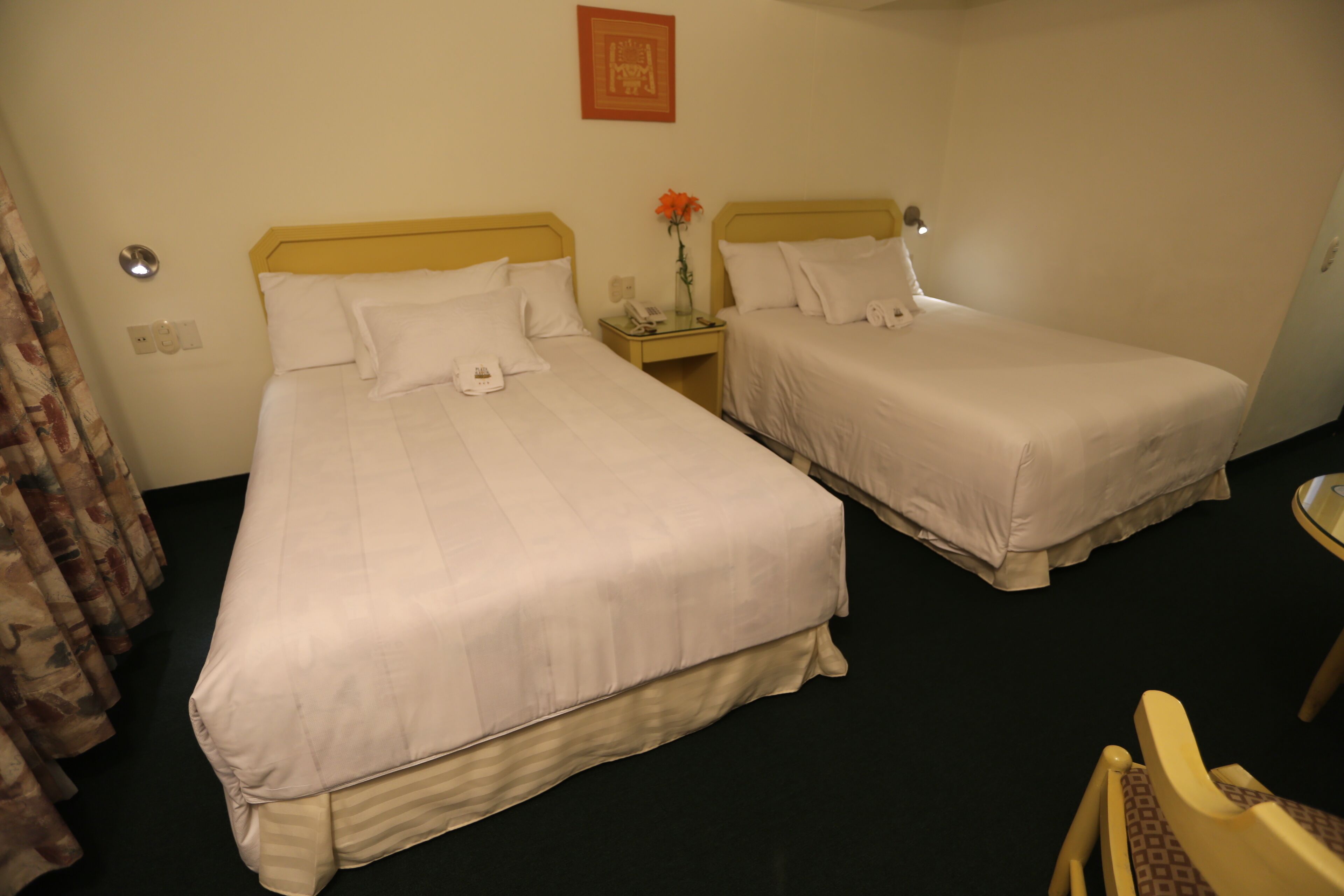 A hotel room with two single beds, a nightstand with a lamp, and a chair.