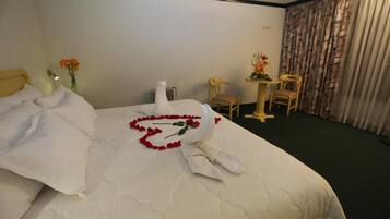 A hotel room with a neatly made bed, a small table with a vase of flowers, and a chair.