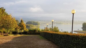 Un chemin de gravier menant à un lac, bordé de lampadaires et d’arbres.