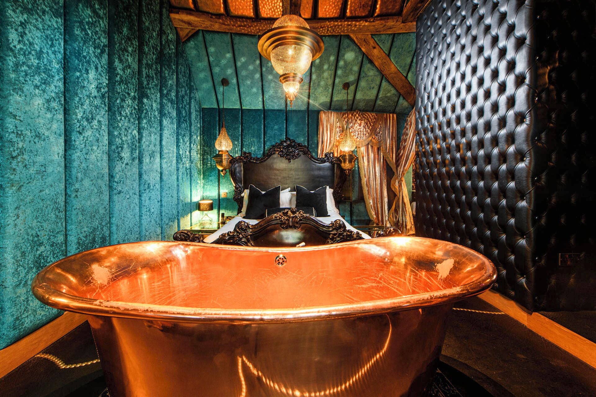 Una bañera de cobre en una habitación con paredes de madera y un cabecero tapizado negro.