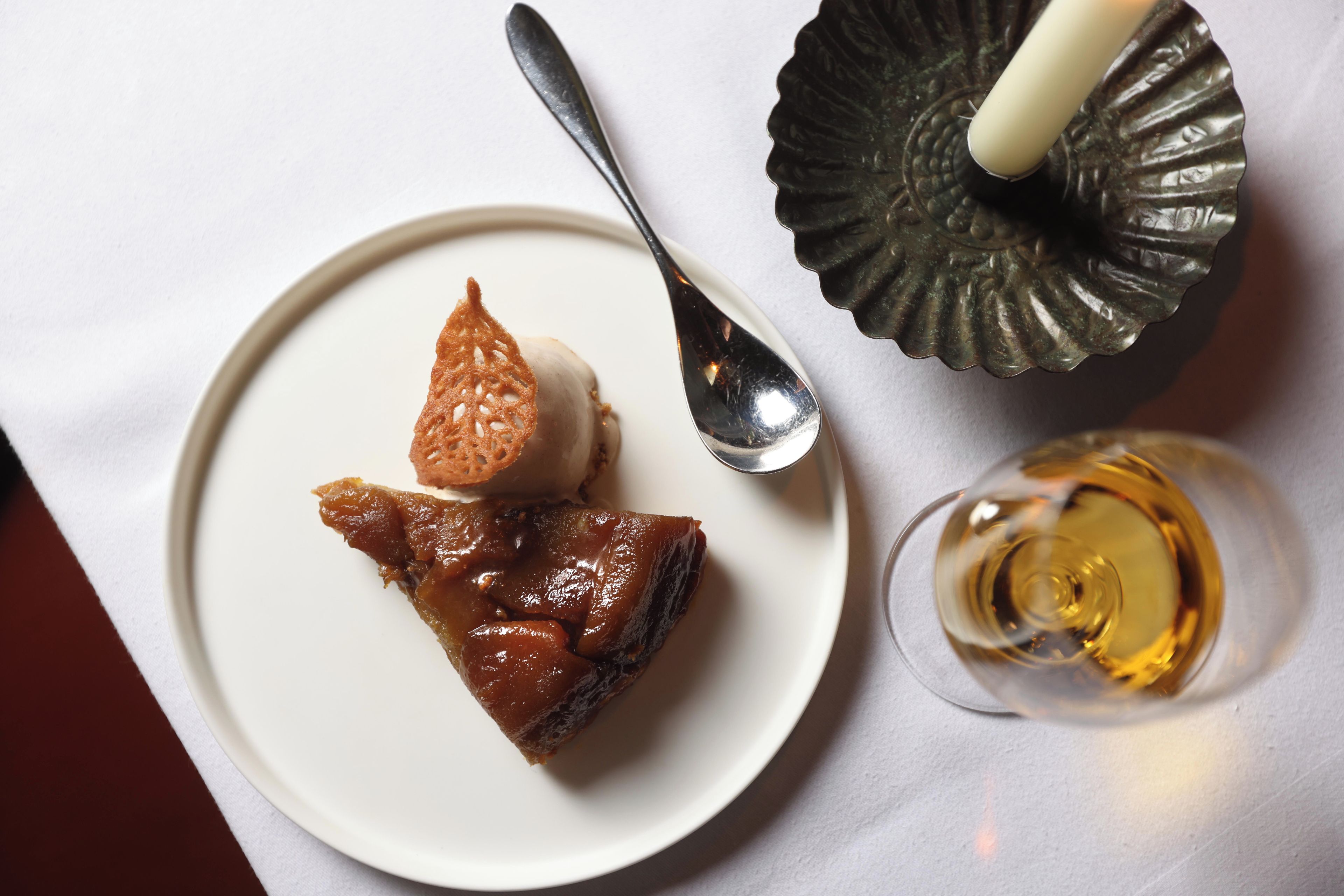 A dessert plate with a spoon and a glass of a yellowish liquid, possibly a beverage.