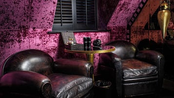 A room with a sloped ceiling, a window with shutters, a round table with two chairs, and a decorative lamp.