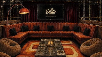 Uma área de estar acolhedora com sofá modular, mesa de centro e uma tela grande exibindo 'The Studio Karaoke & Events'.
