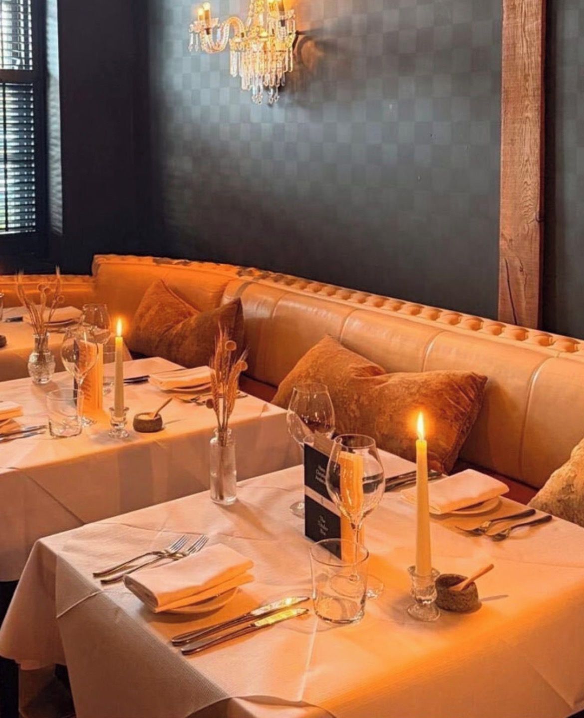 A dining area with a long table set for a meal, a cushioned bench, and a chandelier.