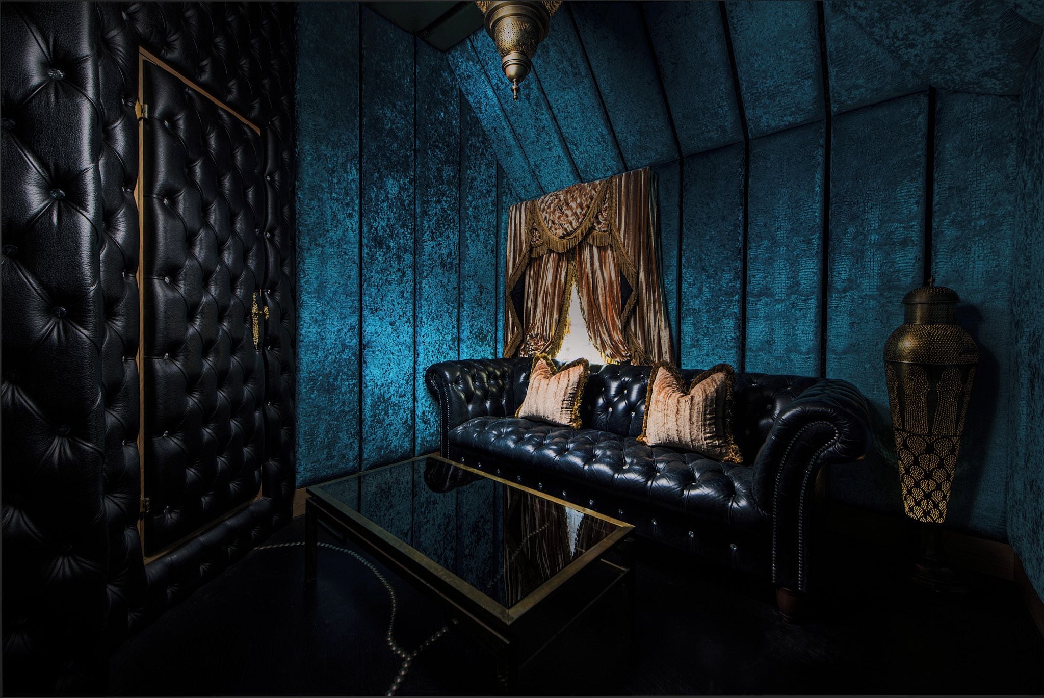 A room with a black leather sofa, a glass coffee table, and a decorative lamp.