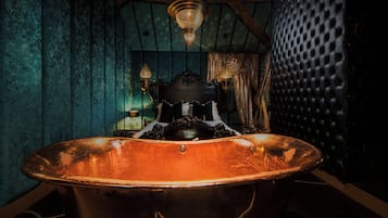 A vintage bathtub with ornate detailing, a wooden ceiling, and a chandelier.