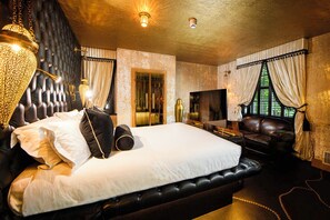 A large bed with a headboard, a television, and a seating area with a leather couch.