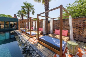 Un espace aménagé au bord de la piscine, avec plusieurs chaises longues en bois, un mur en briques et une piscine à eau claire.