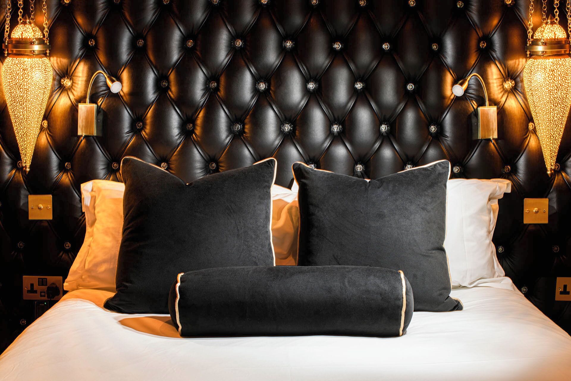 A bed with a tufted headboard, black pillows, and bedside lamps.