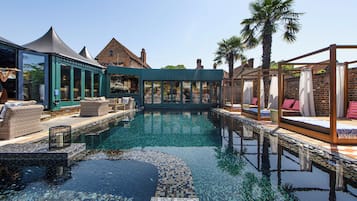 Une piscine avec des espaces de détente, un coin salon abrité et un bâtiment en briques en arrière-plan.