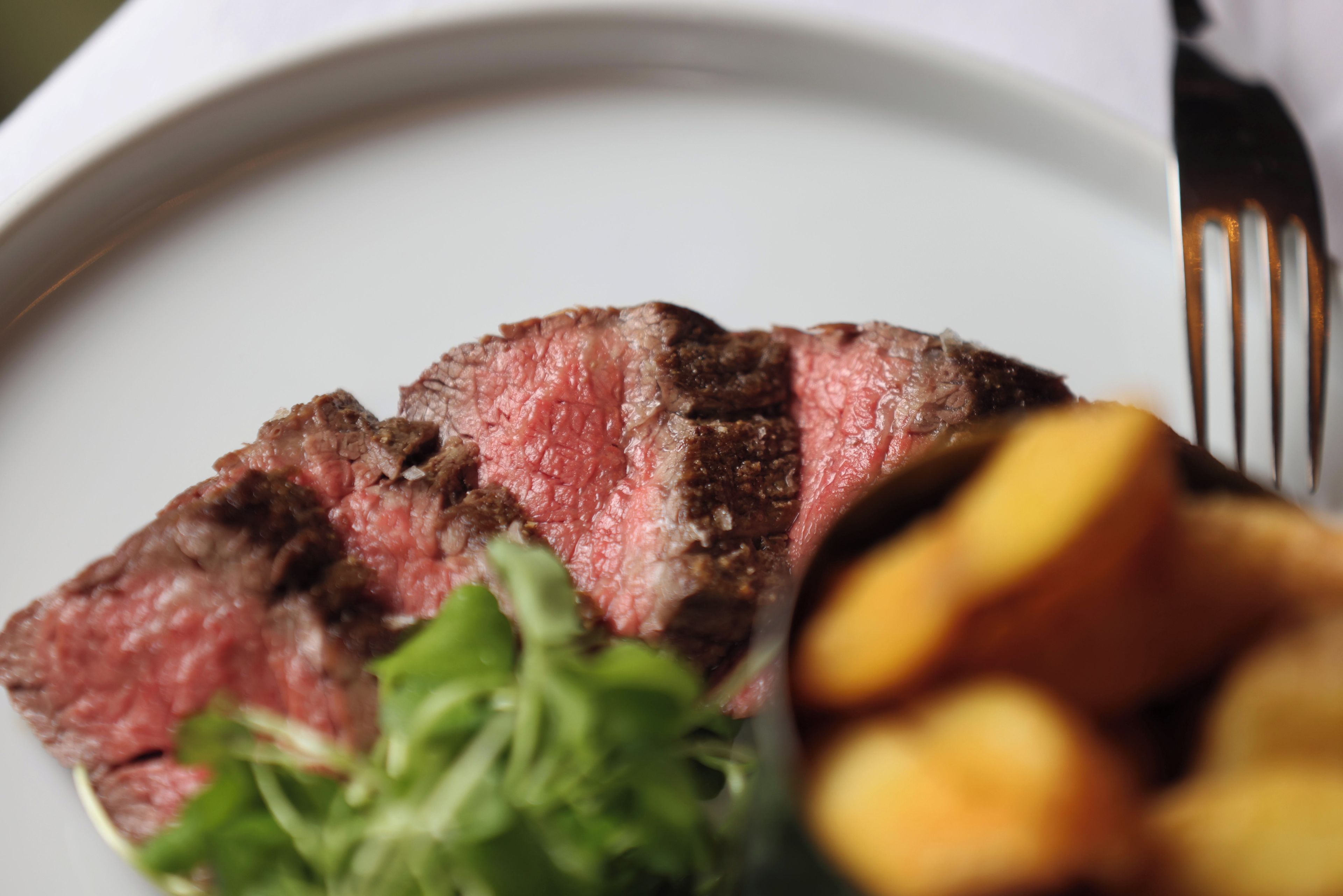 Prato com carne fatiada, vegetais e um garfo.