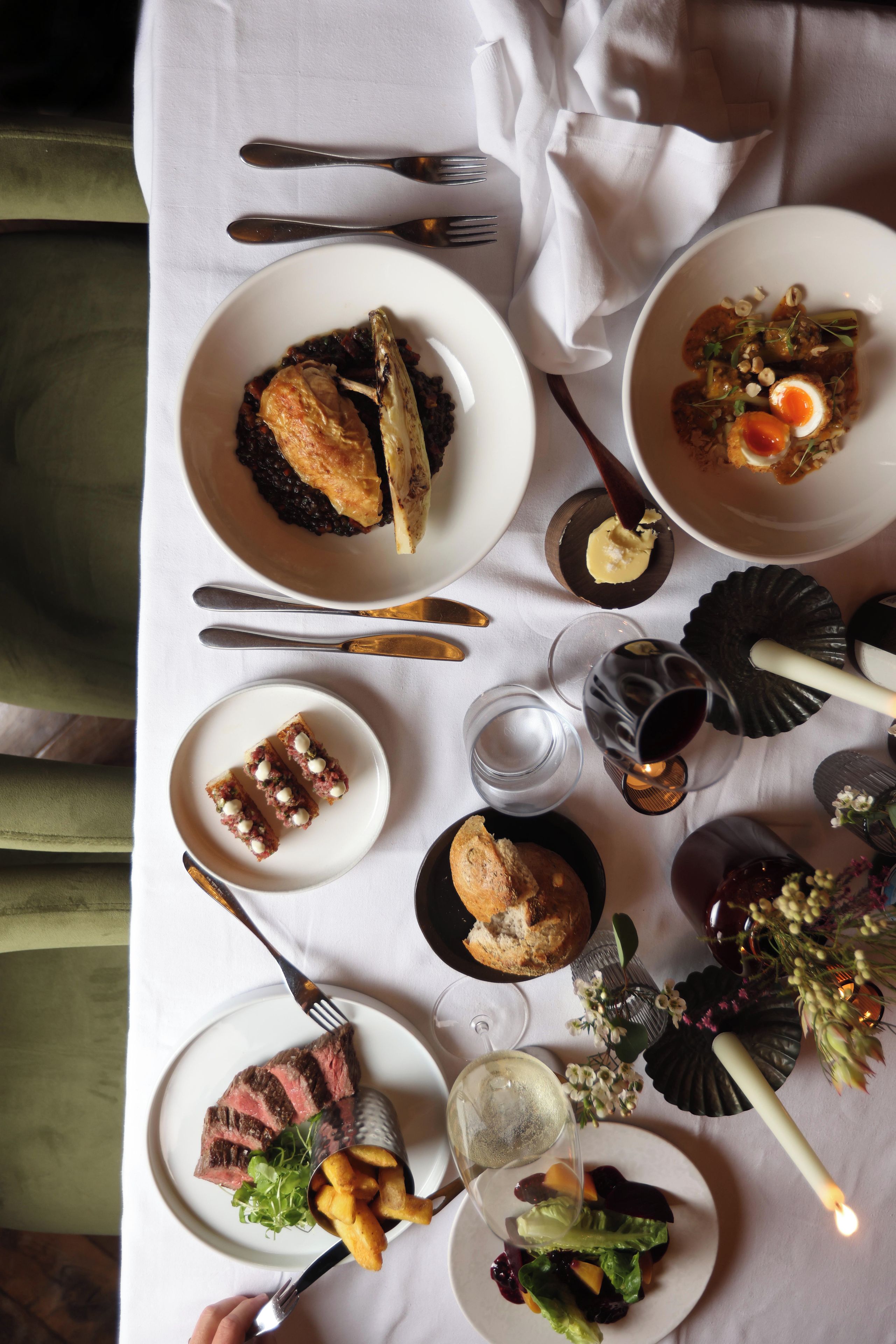 A table set with various dishes, including steak, bread, and a salad, suggesting a meal setting.