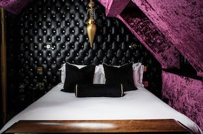 Una cama con cabecera capitonada, una mesita de noche y una lámpara colgante decorativa.