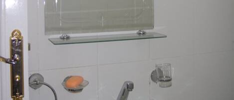 Un baño con lavamanos blanco, cabina de ducha de vidrio y espejo sobre el lavamanos.