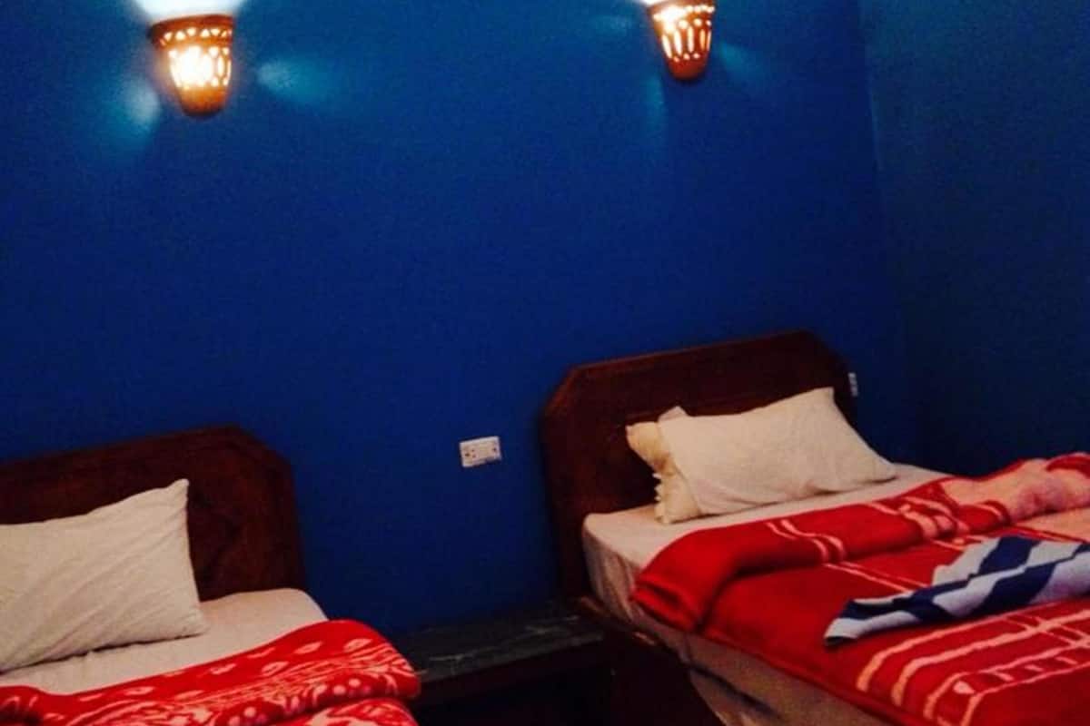Una habitación con dos camas, cada una con un edredón rojo estampado y almohadas blancas. Hay luces fijadas a las paredes azules.