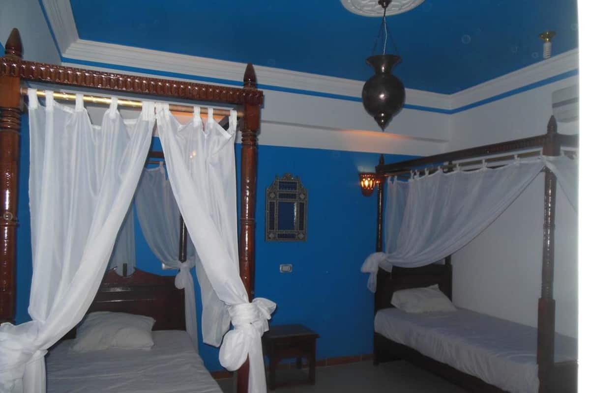 Una habitación con dos camas, cada una con dosel, una mesita pequeña y una lámpara fijada a la pared.
