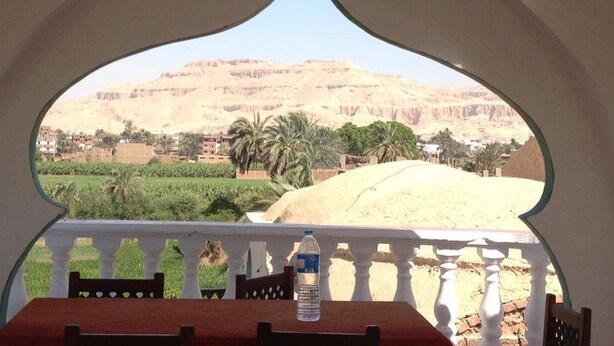A view from a balcony with a table and chairs, overlooking a desert landscape with mountains and palm trees. - Cleopatra Hotel Luxor (Luxor)