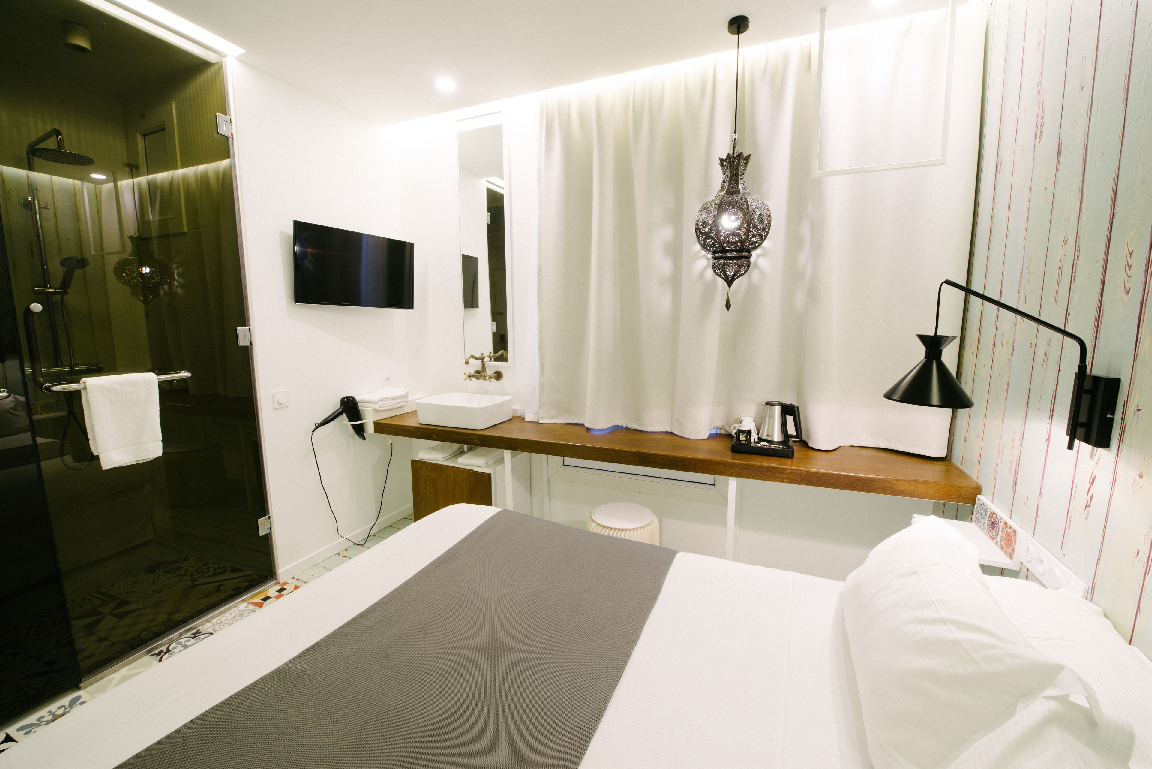 Una habitación de hotel moderna con ducha, tocador con espejo, mesita de noche y cama con ropa blanca.