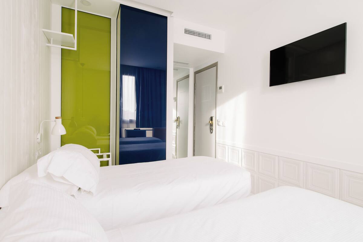Una habitación de hotel con una cama, un televisor montado en la pared y una puerta que da a otra habitación.