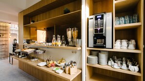 A buffet setup with various food items, a coffee machine, and glassware on wooden shelves. - Atypik Hôtel - Urban Style (Clichy)