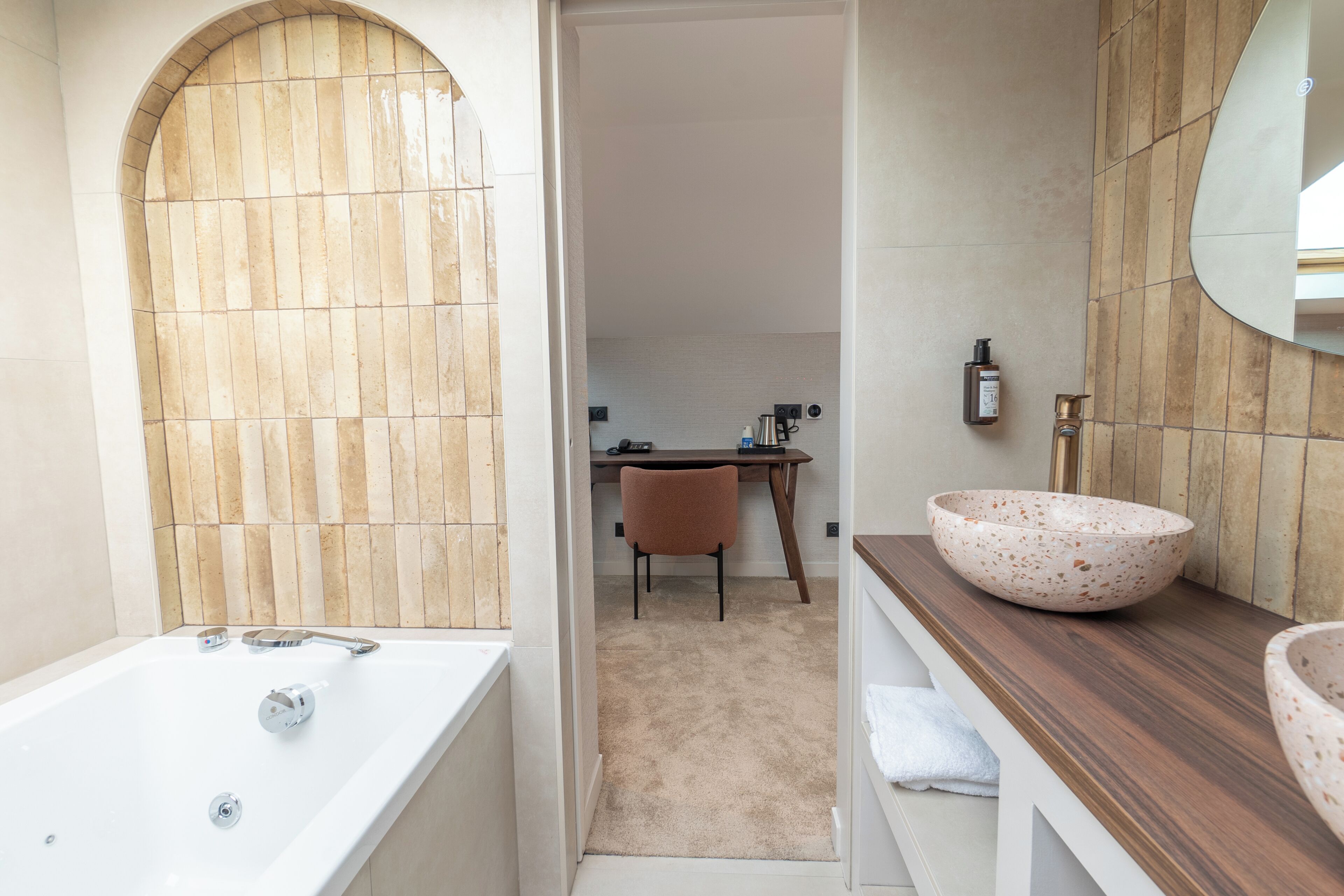 A bathroom with a bathtub, a wooden vanity, and a desk with a chair.