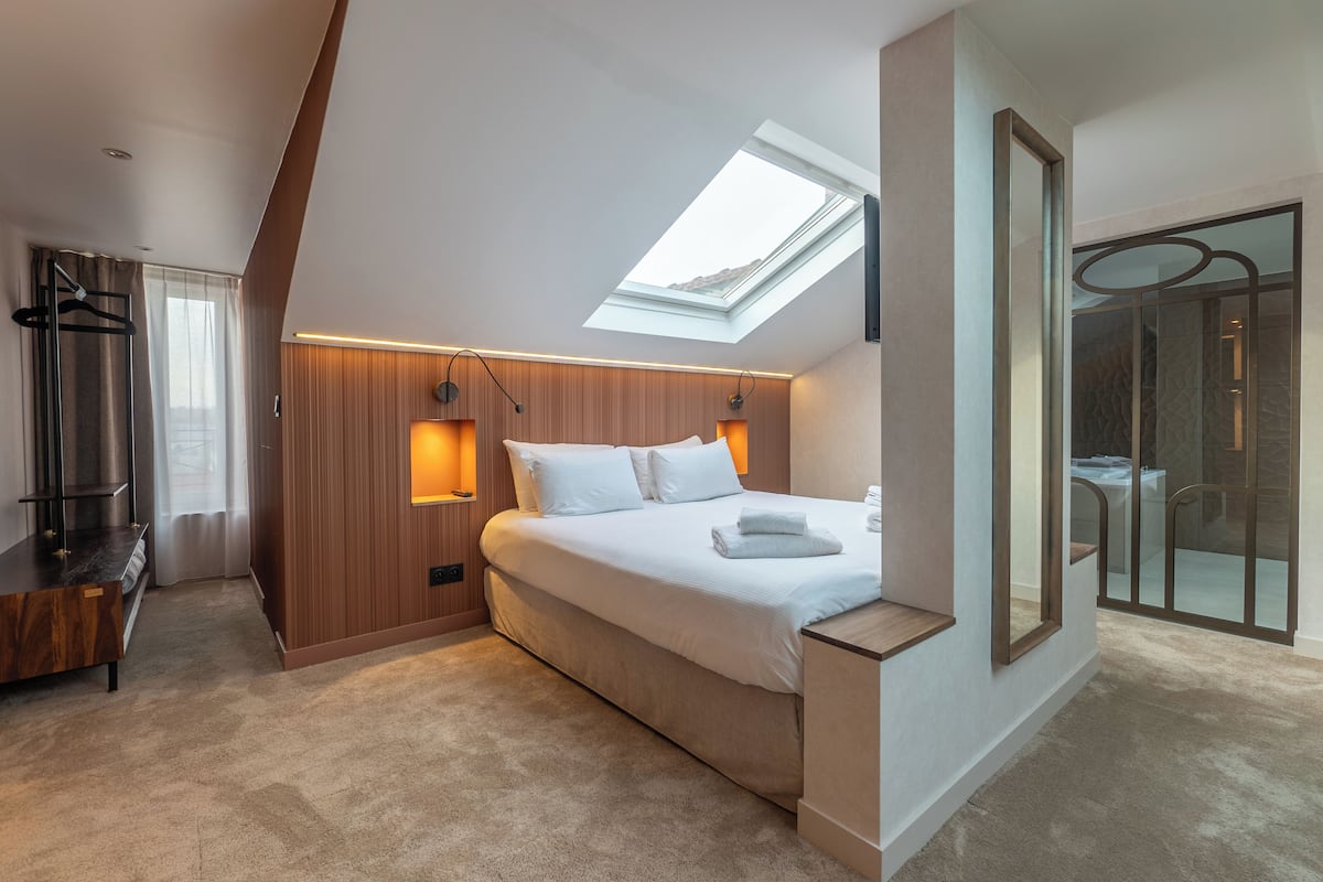 Un dormitorio moderno con tragaluces, un panel de pared de madera, una cama con ropa de cama blanca y un banco empotrado.