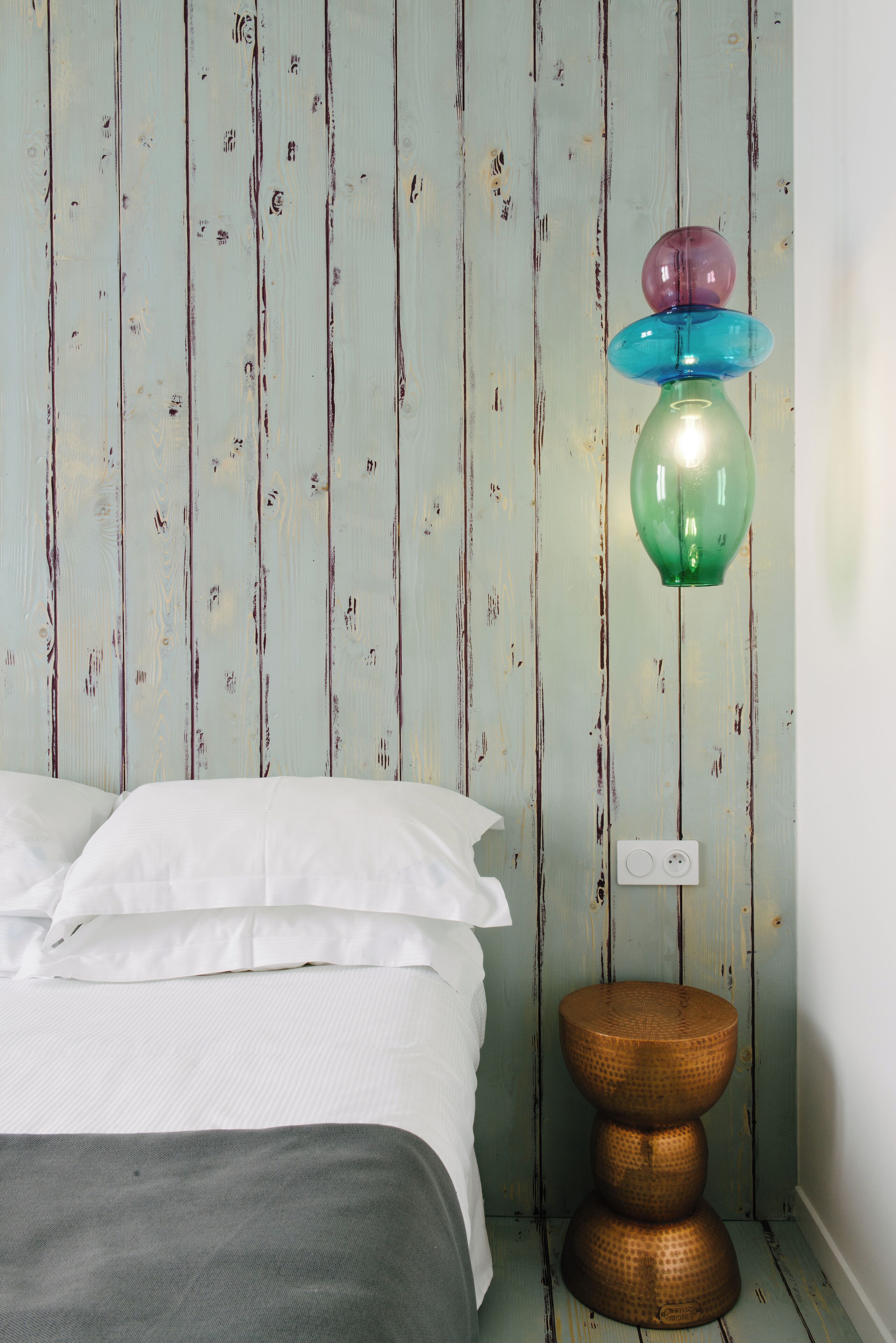 A bedroom with a bed, a wall-mounted lamp, and a textured wall.