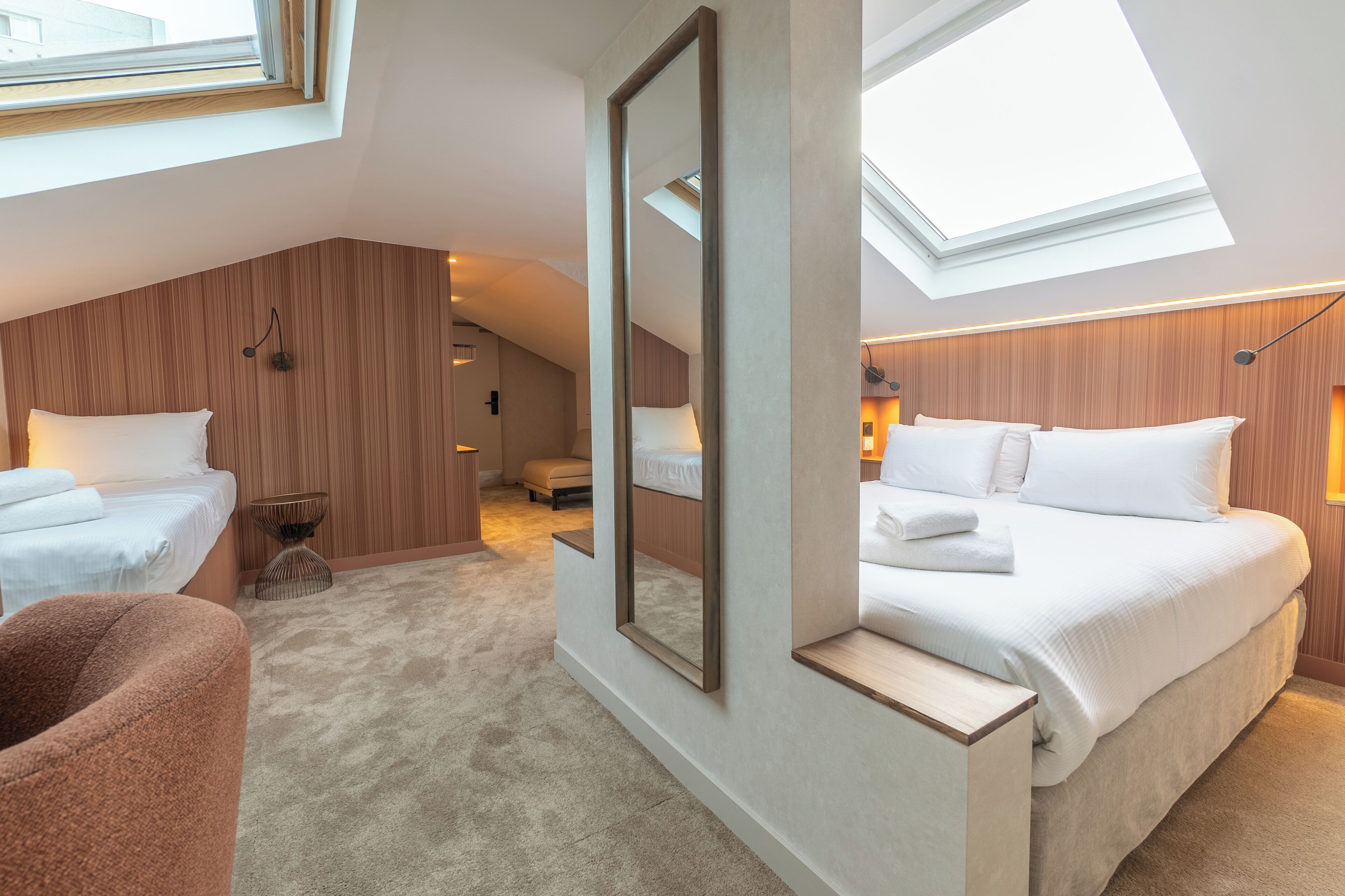 Une chambre d’hôtel moderne dotée d’une lucarne, d’un grand lit, d’un lit plus petit et d’un coin salon.