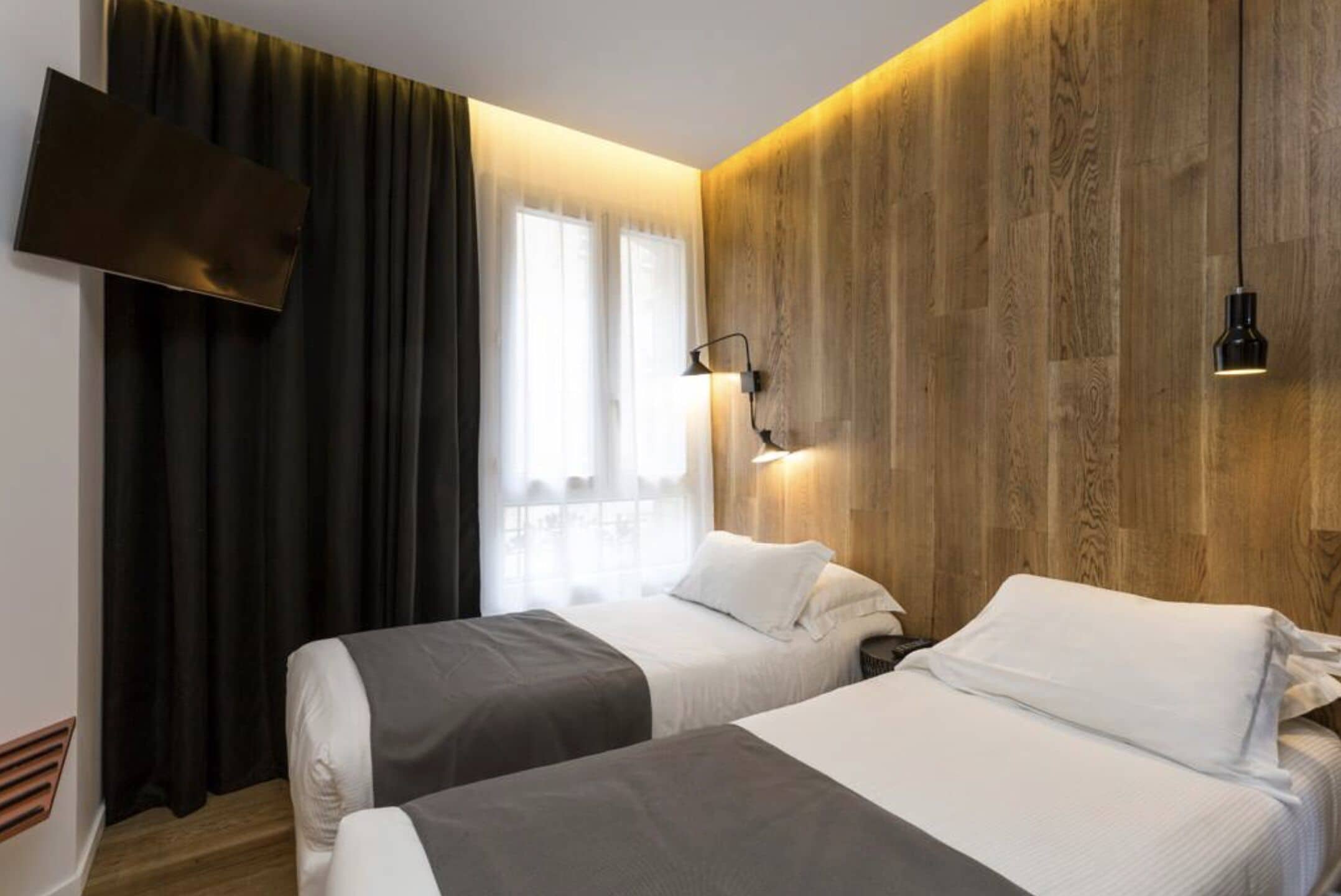 A hotel room with two beds, a TV mounted on the wall, and a wooden accent wall.