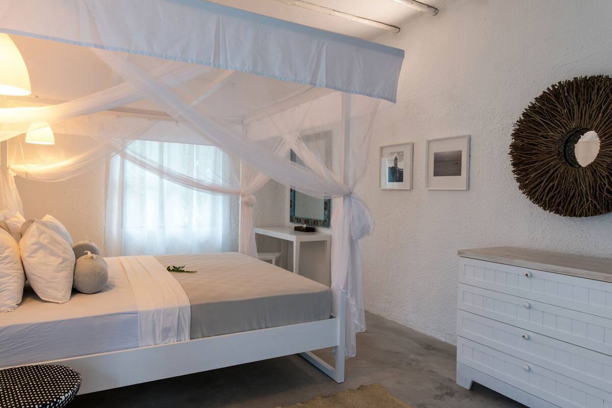 A bedroom with a canopy bed, a desk, a dresser, and wall-mounted decor.