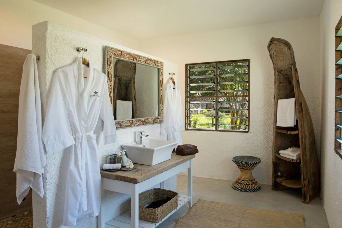 A bathroom with a white sink, mirror, and wooden vanity. There are towels and a brown bag on the vanity.