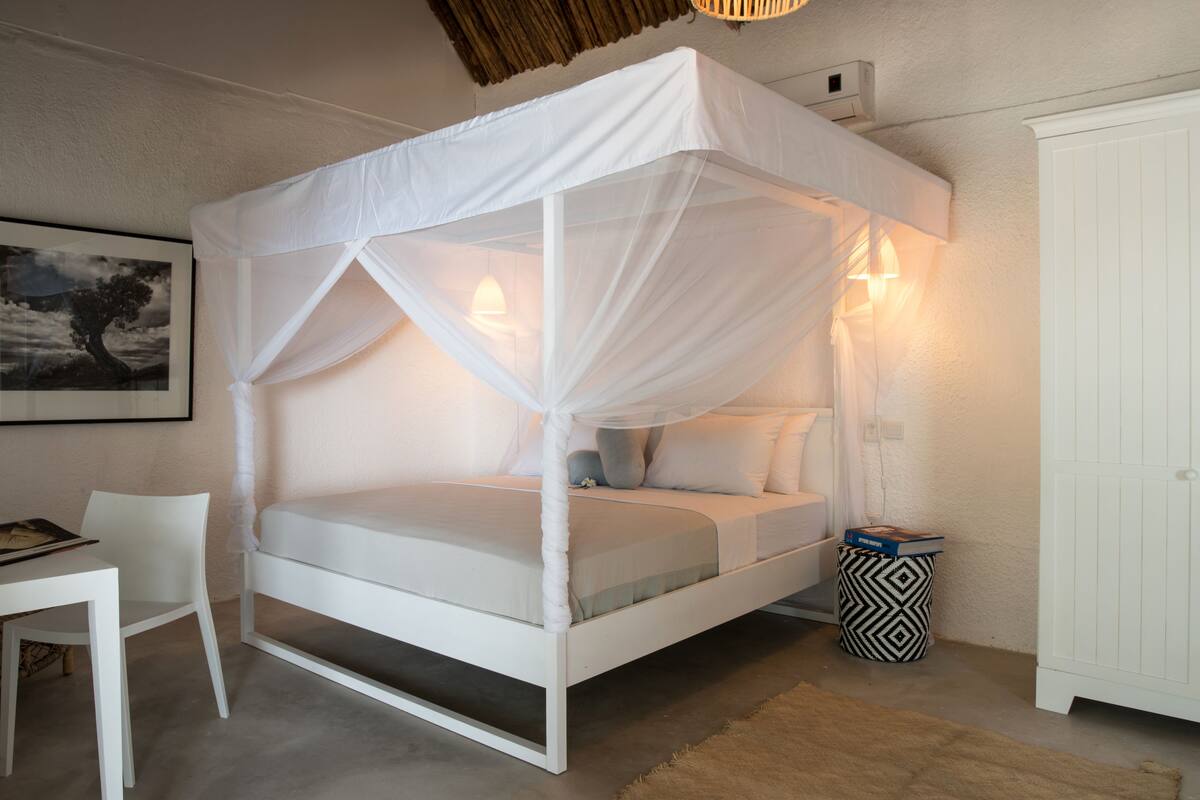 Ein weißes Himmelbett mit Baldachin, ein Nachttisch, ein Sessel, ein gemusterter Mülleimer und ein Kleiderschrank.