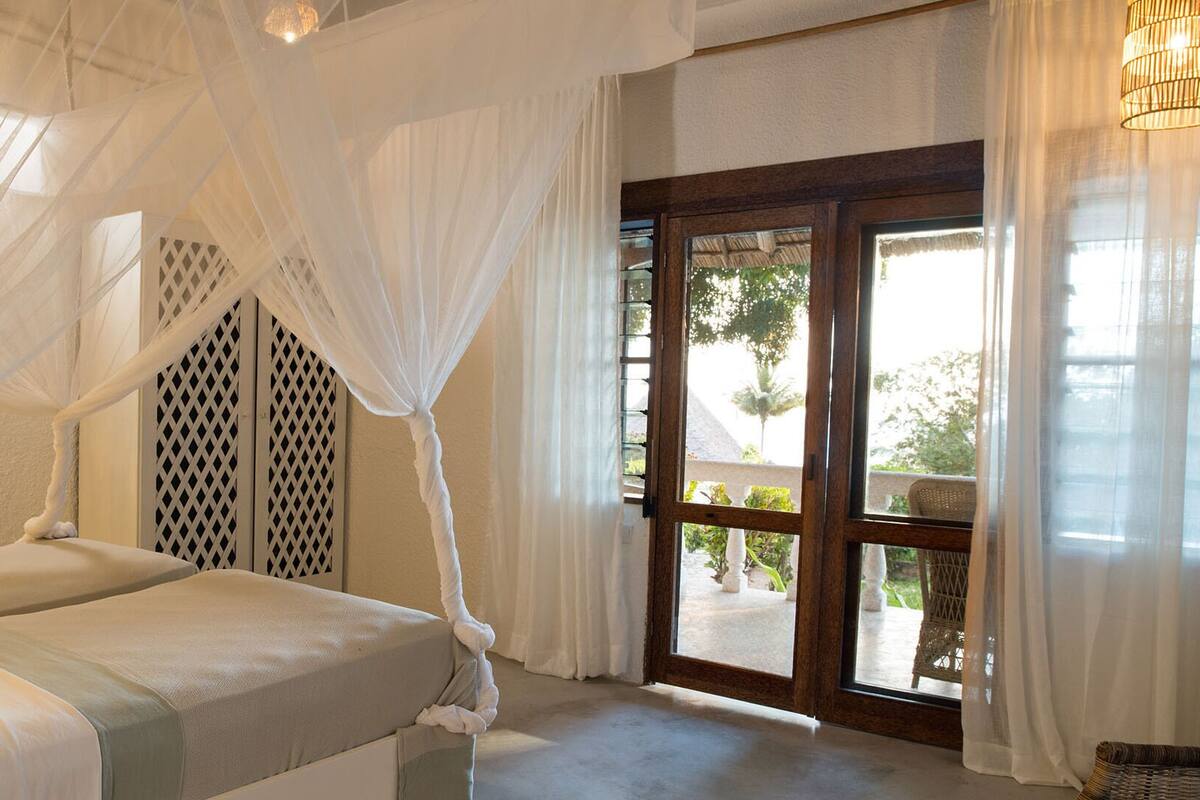 Ein Schlafzimmer mit Baldachinbett und Blick ins Freie, mit einer Holztür.
