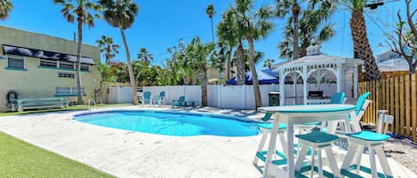 A backyard with a swimming pool, a gazebo, and palm trees.
