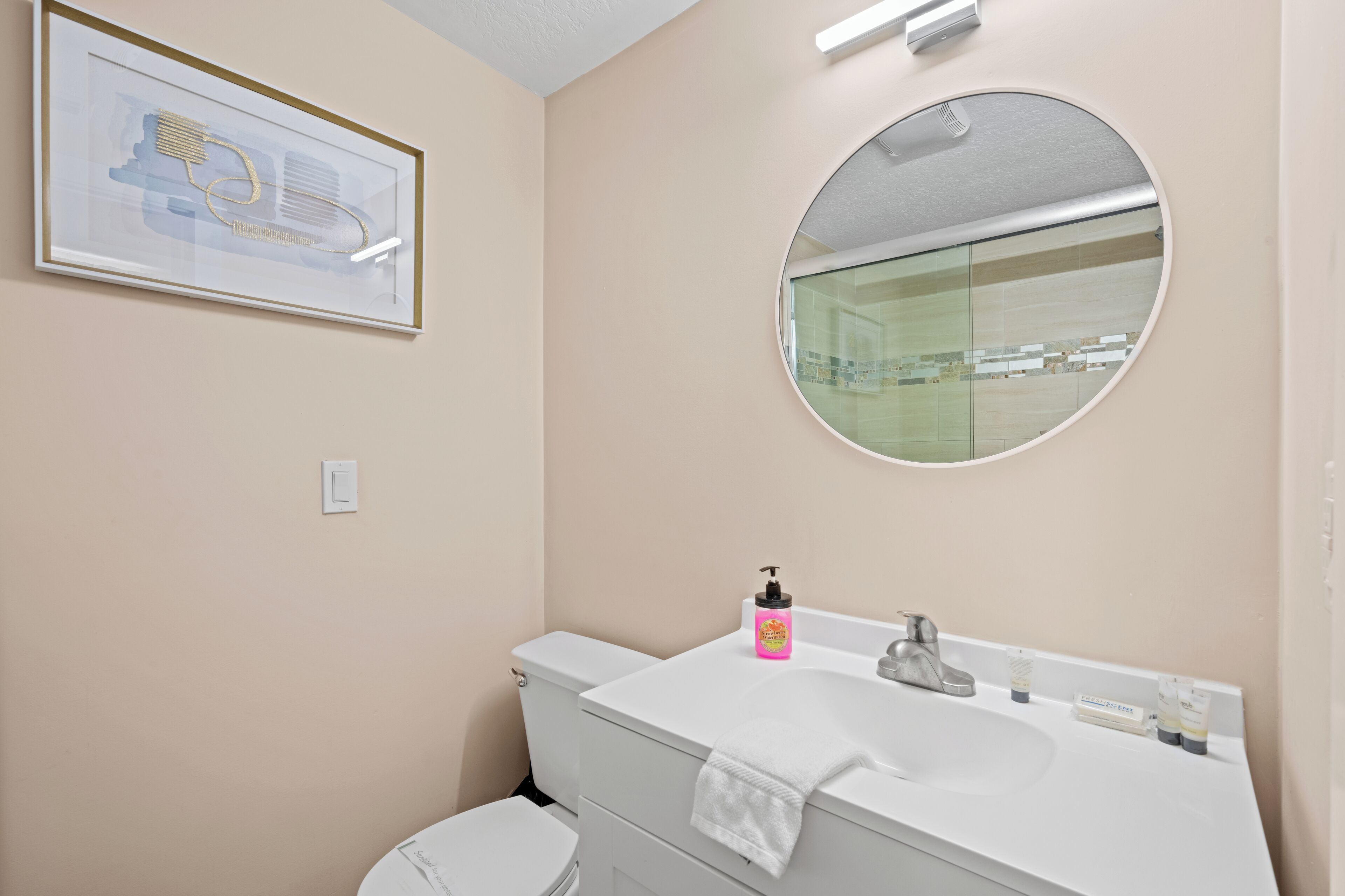 A bathroom with a white sink, a round mirror, and a framed artwork on the wall.