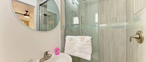 A bathroom with a round mirror, a sink, and a glass shower enclosure.