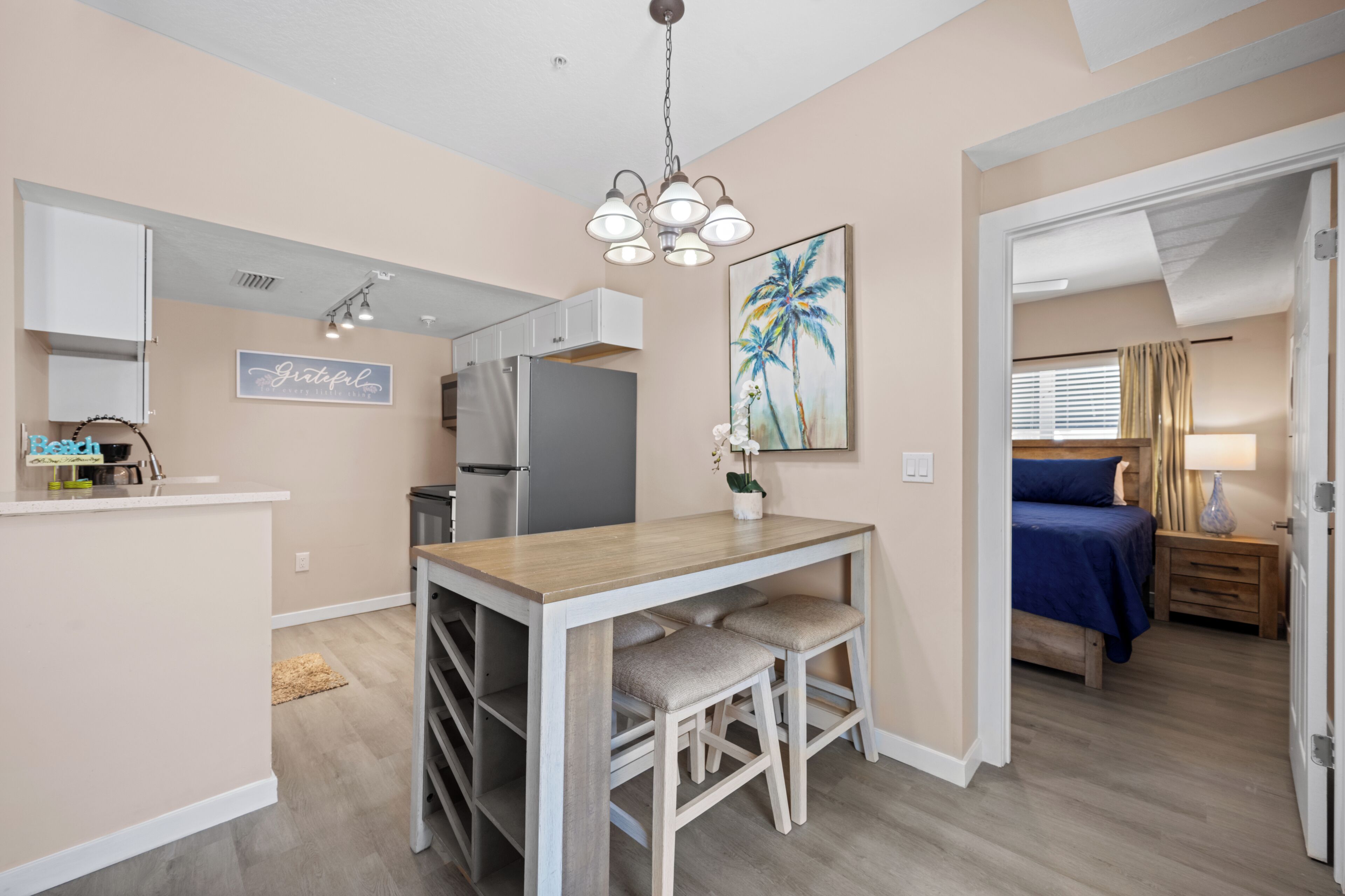 Un espacio habitable compacto con kitchenette, un comedor con mesa y sillas de madera, y un dormitorio con cama y mesita de noche.