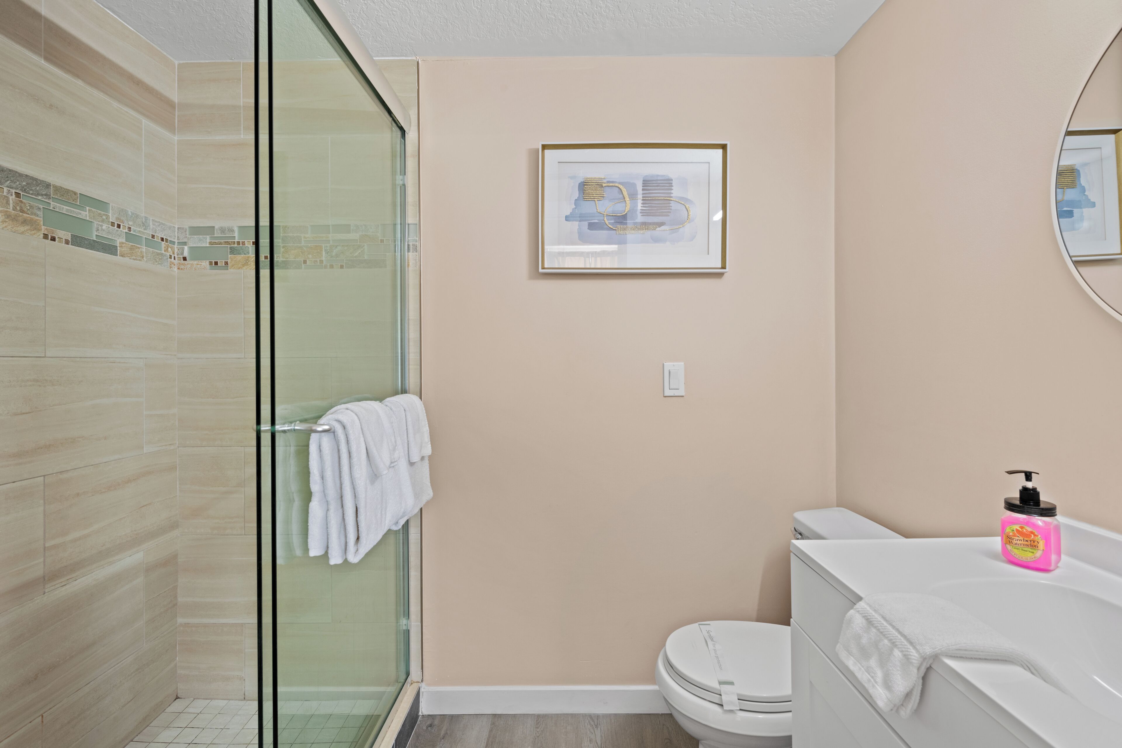 Une salle de bain avec une douche à parois de verre, des toilettes et un lavabo équipé d’un distributeur de savon.