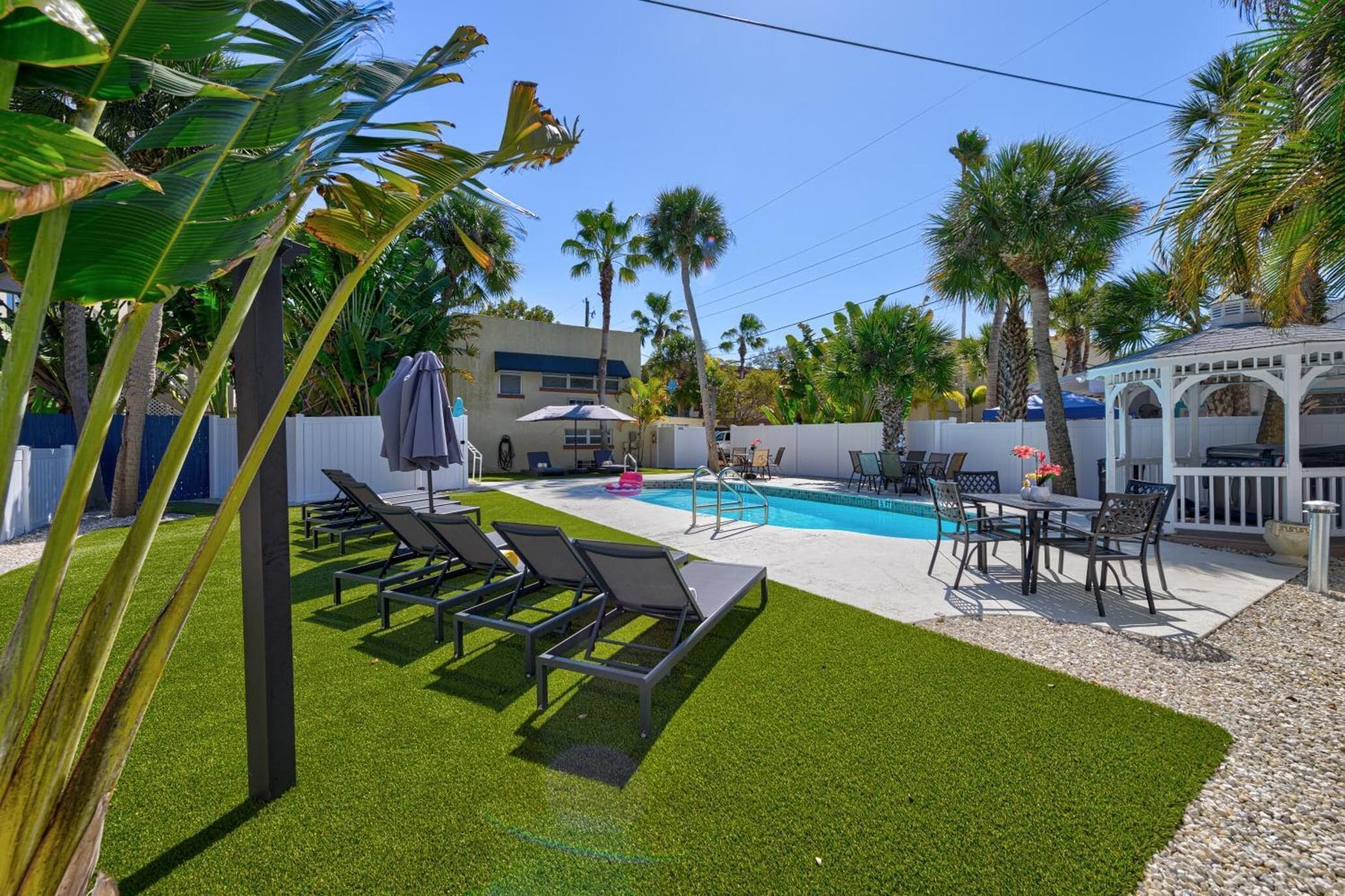 A backyard with a swimming pool, lounge chairs, a table with chairs, and a gazebo.
