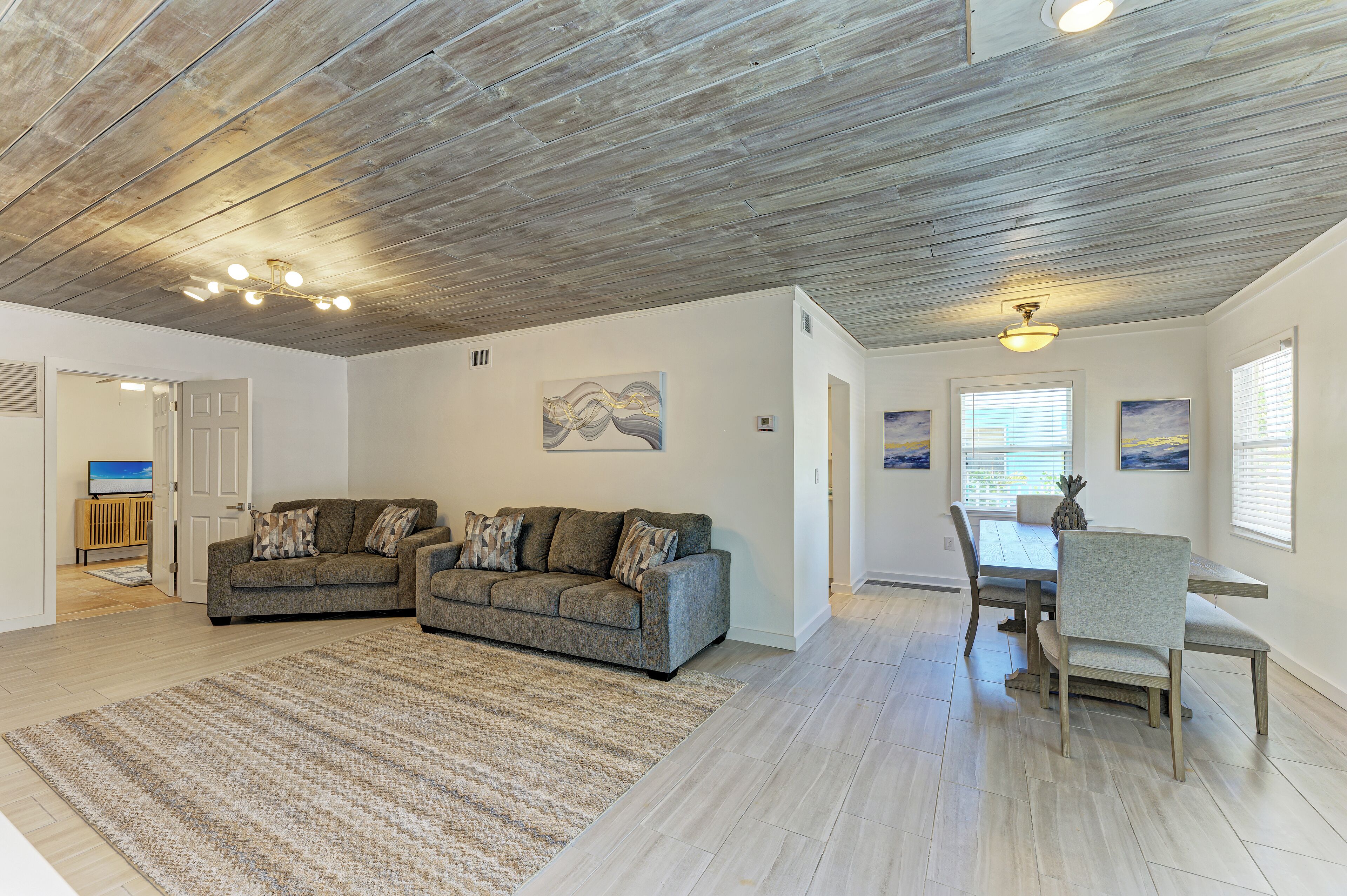 A spacious living area with a wooden ceiling, two sofas, a dining table with chairs, and artwork on the walls.