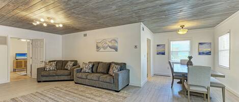 A spacious living area with a wooden ceiling, two sofas, a dining table with chairs, and artwork on the walls.
