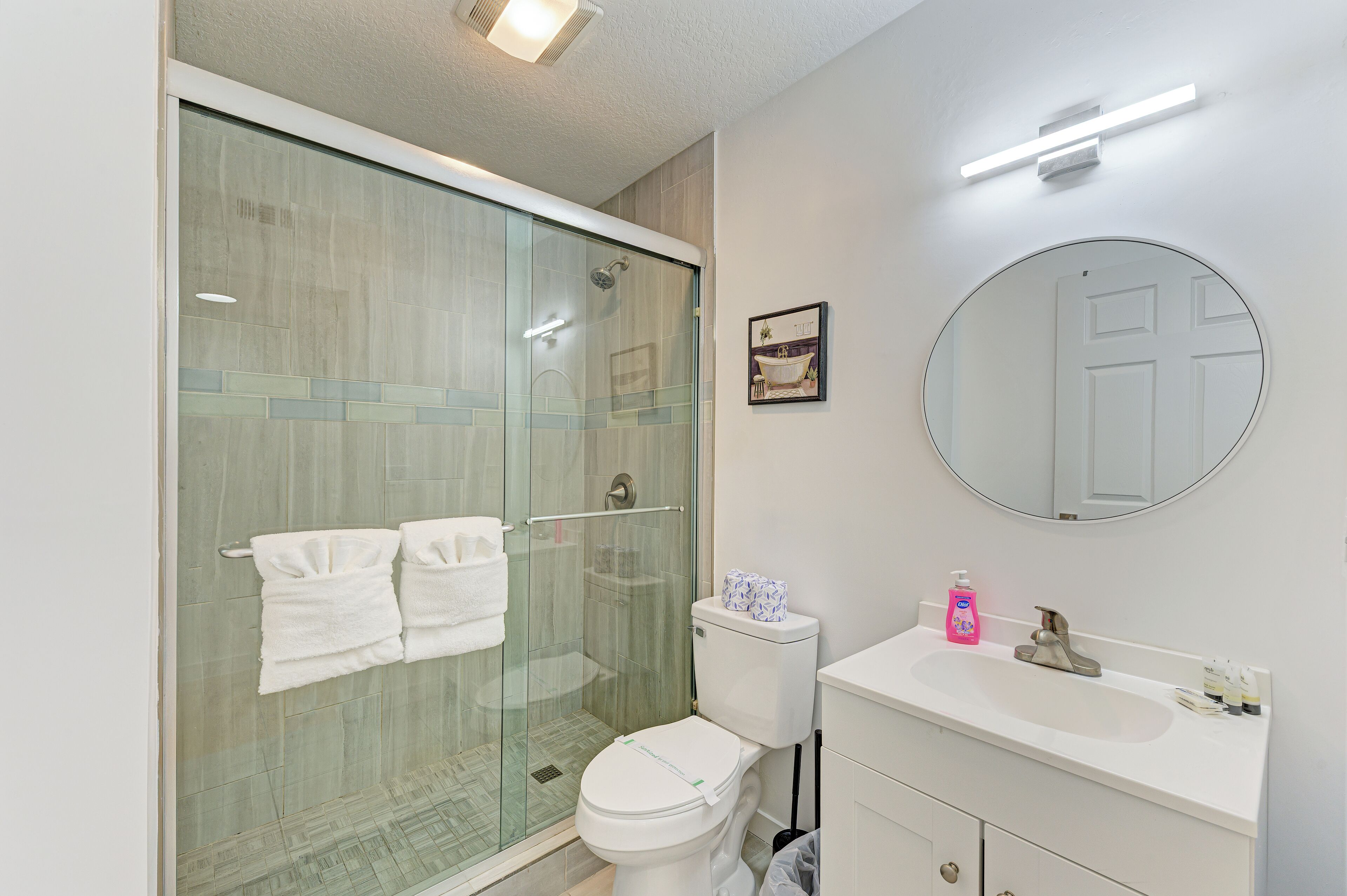 Une salle de bain moderne avec une douche à parois de verre, des toilettes, un lavabo équipé de produits de toilette et un miroir.