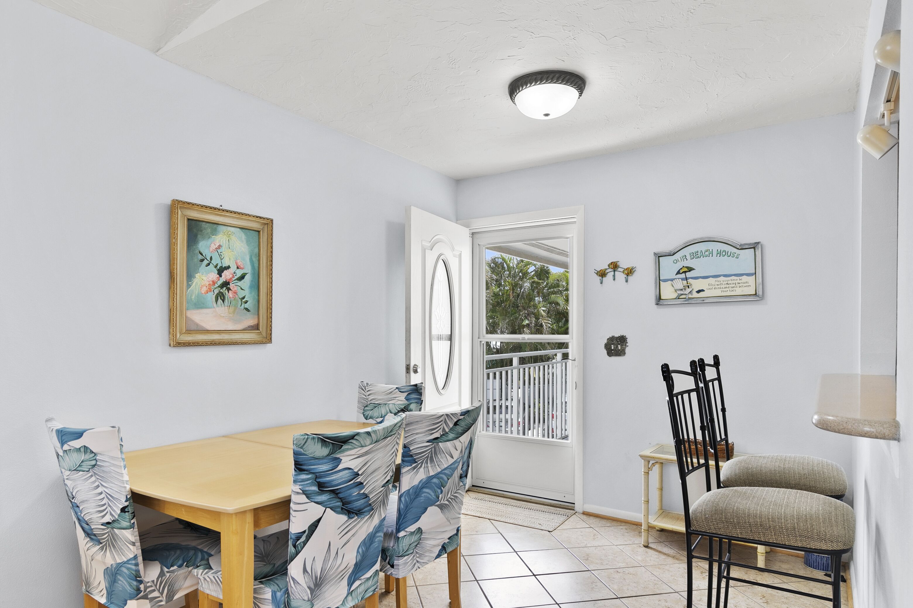A dining area with a wooden table and chairs, a white door leading outside, and a small table with a lamp.